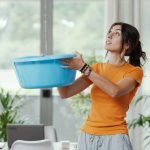Young upset woman collecting water leaking and dripping from the ceiling