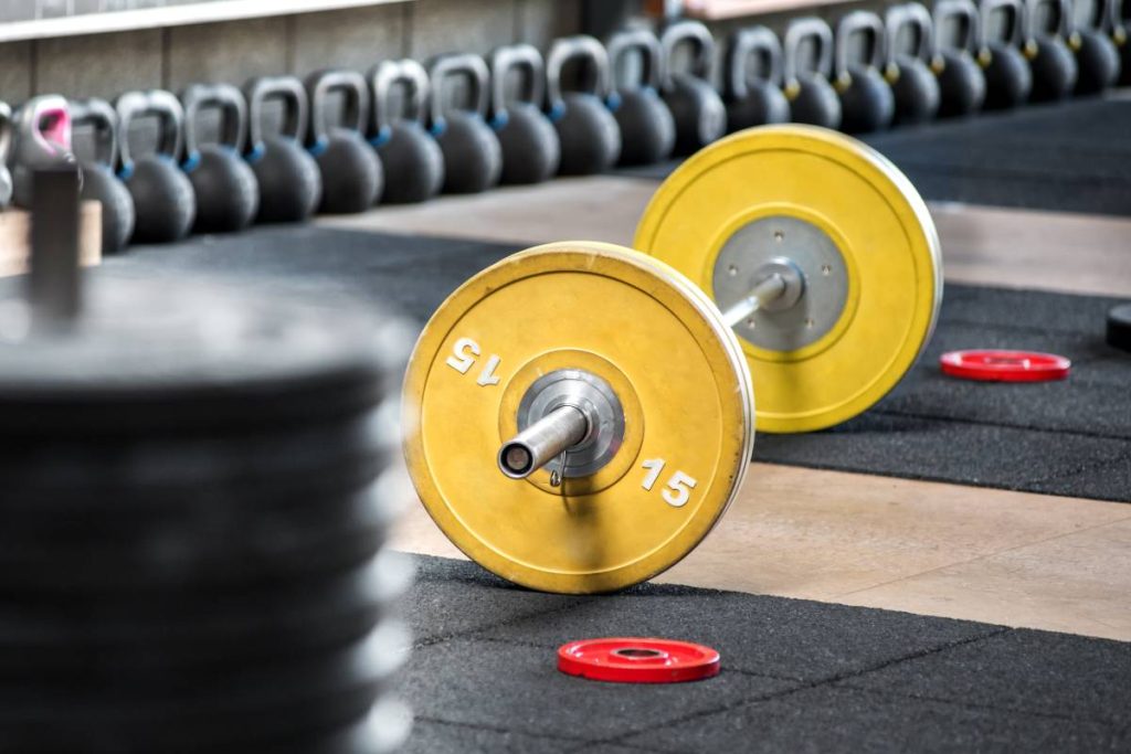 Yellow barbell on the floor in gym, viewed from the side in selective focus. Heavy weights training equipment