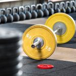 Yellow barbell on the floor in gym, viewed from the side in selective focus. Heavy weights training equipment