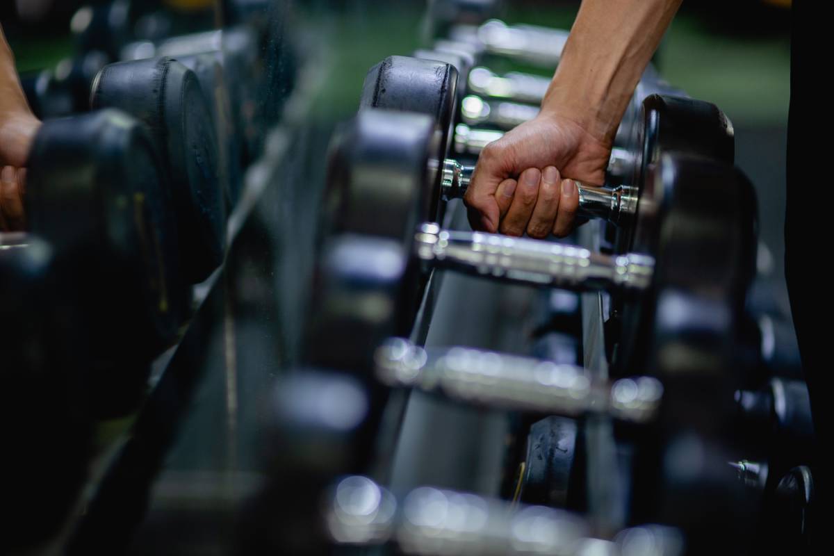 Close up hand of young man holding dumbbell after choosing one in row for exercise at fitness gym, copy space