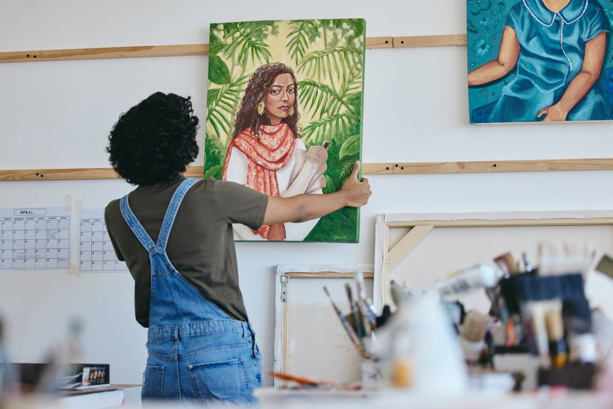 Woman artist, painter and hanging canvas on wall for exhibition to display in studio, art gallery o.