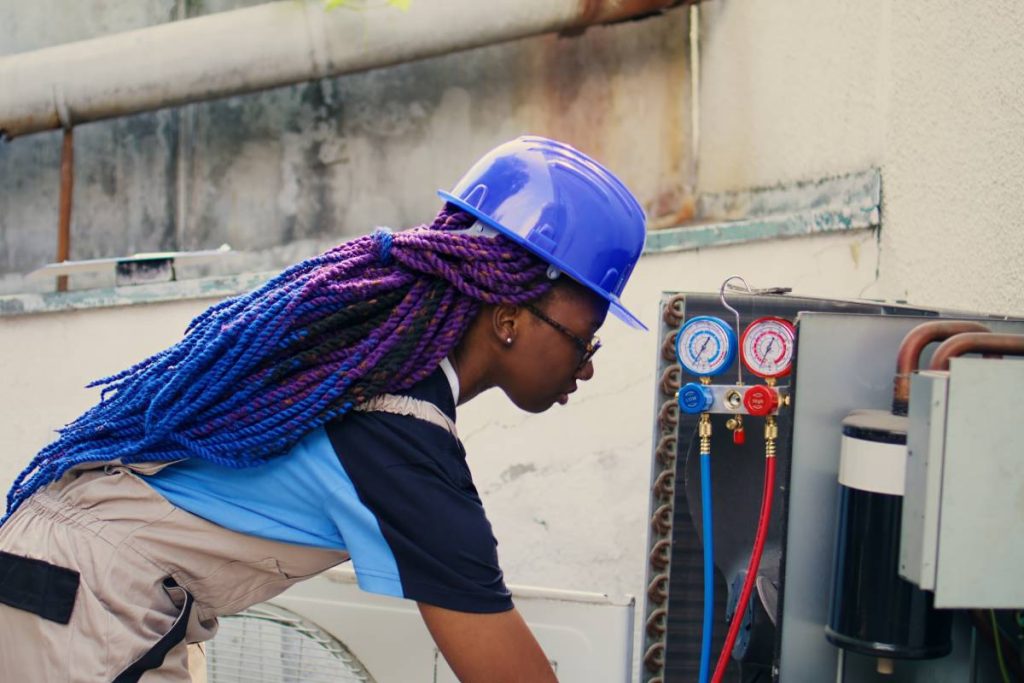Close up portrait of smiling african american electrician mounting manometer used for checking condenser freon tank in need of repairing. Engineer using manifold gauges to check refrigerant levels