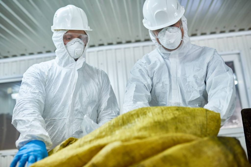 Low angle portrait of two workers wearing biohazard suits working at waste processing plant sorting recyclable materials on conveyor belt