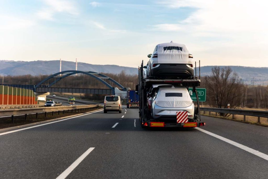 Tow truck car carrier semi trailer on highway carrying batch of new wrapped electric SUVs on motorway road at sunset evening time. Business distribution logistics service. Lorry driving highway.