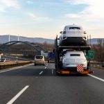Tow truck car carrier semi trailer on highway carrying batch of new wrapped electric SUVs on motorway road at sunset evening time. Business distribution logistics service. Lorry driving highway.