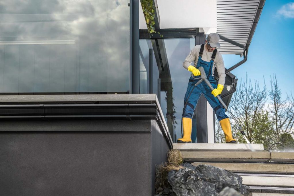 Caucasian Men in His 40s Cleaning Backyard Garden Concrete Paths Using Powerful Pressure Washer.