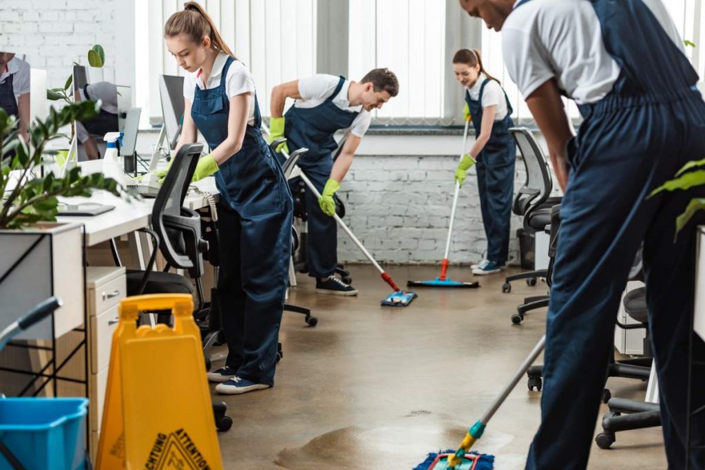 multicultural team of young cleaners washing floor with mops in office