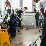 multicultural team of young cleaners washing floor with mops in office