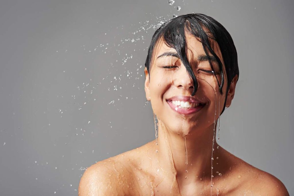 Studio shot of a young woman enjoying a shower against a gray background.