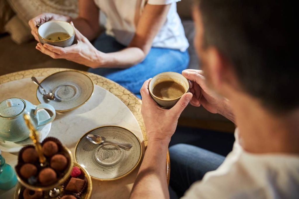 Cropped photo of brunette man holding cup of coffee and spending tea with his girlfriend