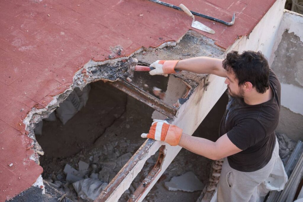 Young man tearing the roof of a house down using a mallet.